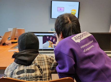 A student coding Python on a laptop in class.